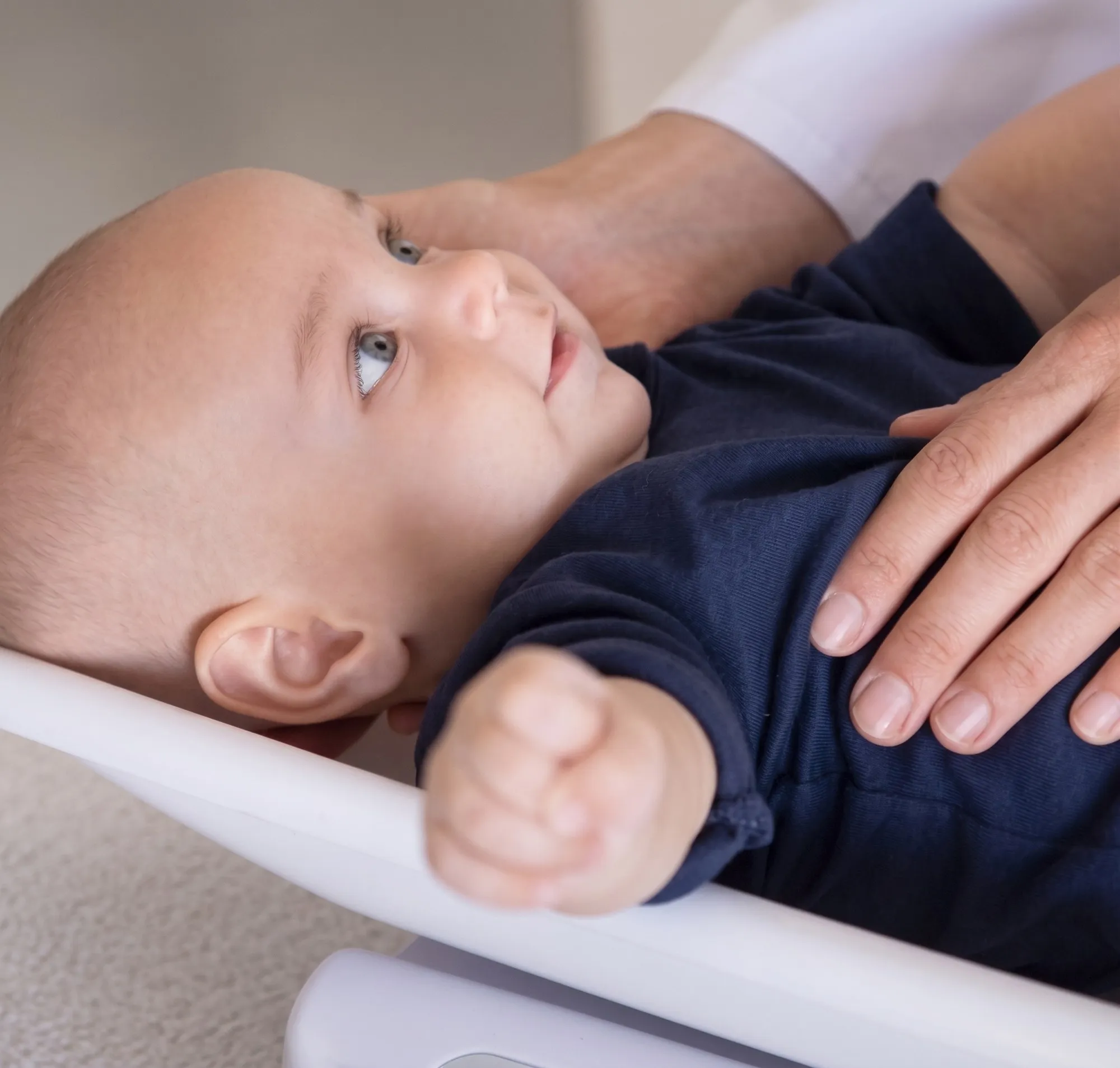 Bebê deitado no trocador olhando para cima, com a mão da médica sobre a barriga