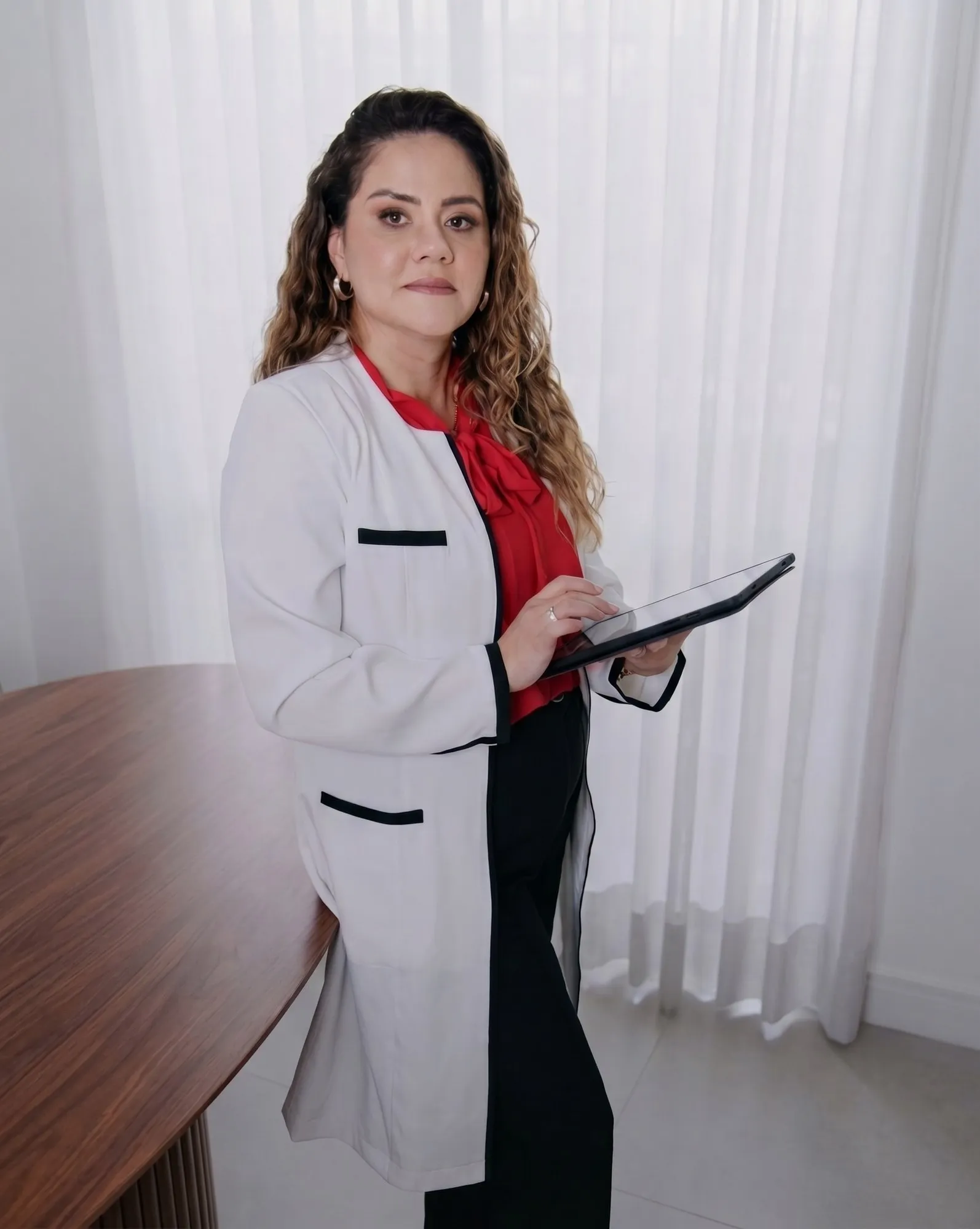 Dra. Gigliola Peláez, de jaleco, em pé segurando uma prancheta no consultório